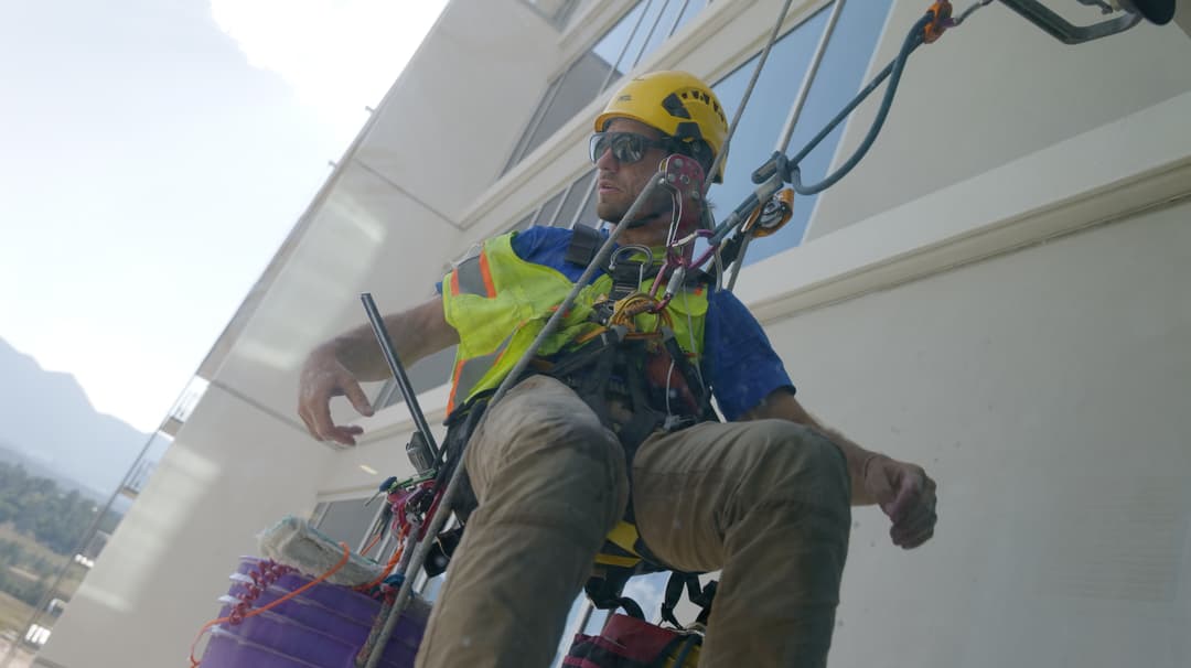 Window cleaner in safety gear using harness and ropes to clean a high-rise building.