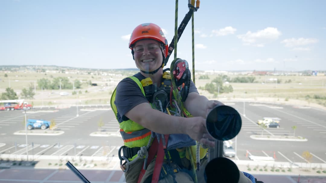 Rope access technician smiling while performing maintenance on a high-rise building.