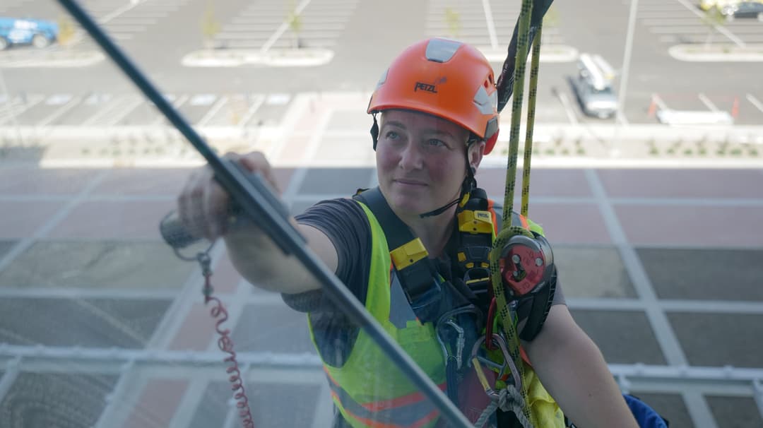 Window cleaner in helmet and safety gear cleaning a skyscraper with harness.