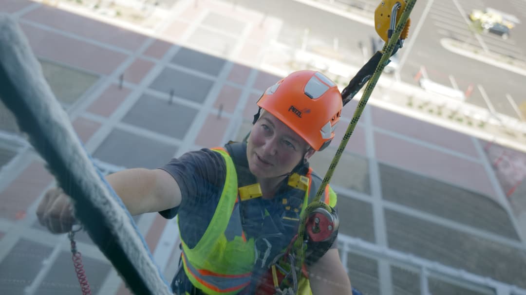 Window cleaner in safety gear scaling a high-rise building, focused on the task.
