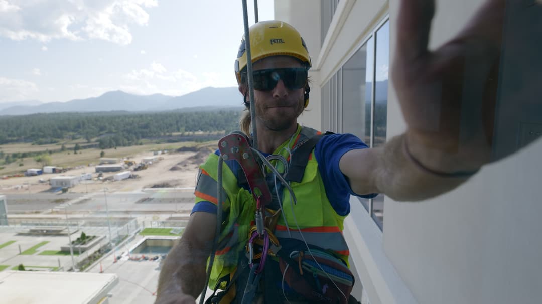 Window cleaner in safety gear working on a high-rise with mountain view in the background.