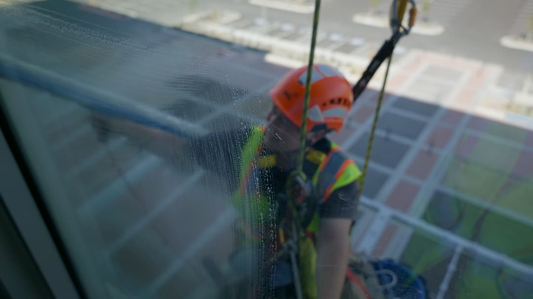 Window cleaner in safety gear using ropes to clean glass on a high-rise building.