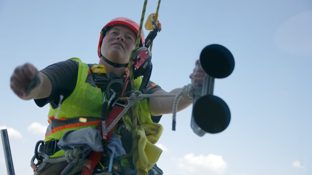 Worker in safety gear using equipment while performing maintenance high above ground.