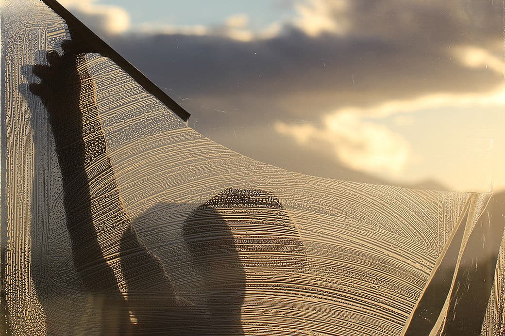 Person cleaning a window with a squeegee against a sunset background.