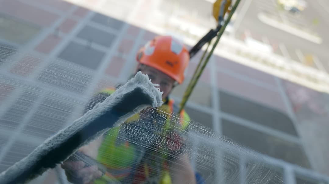 Window cleaner in safety gear washing tall building glass from a suspended harness.