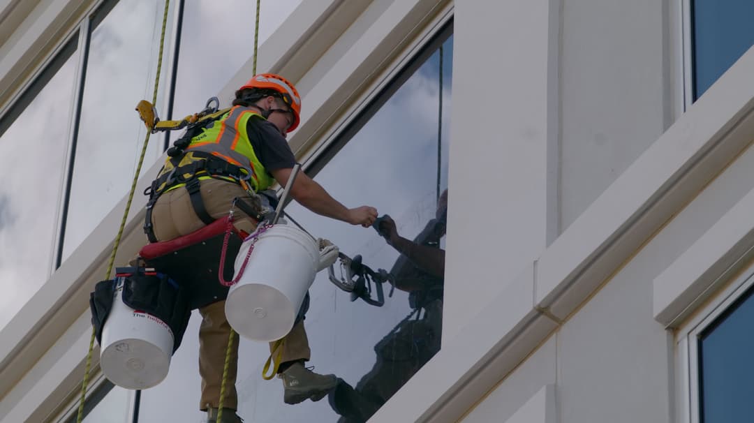 Window cleaner in safety gear cleaning a high-rise building's glass exterior.