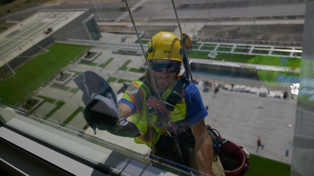 Window cleaner on a building facade using safety gear and equipment for maintenance.