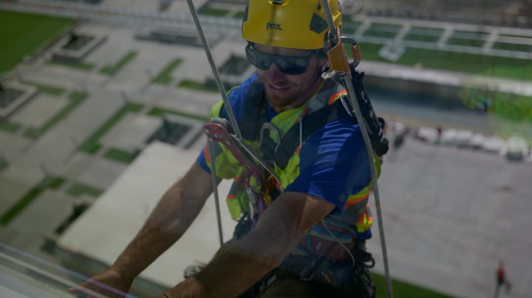 Roofer in safety gear cleaning windows of a tall building with harness and safety equipment.